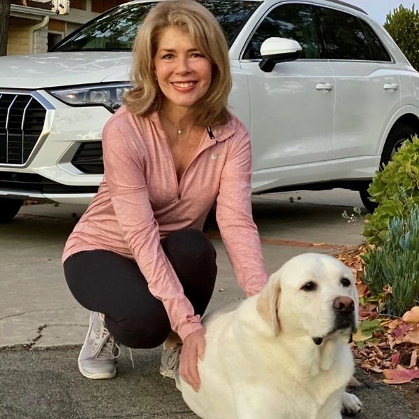 Woman in pink jacket posing with a white Labrador and white car